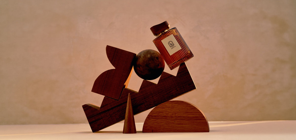 Maison Ormuth reed diffuser vessel resting on a stack of carved walnut blocks against a plaster wall