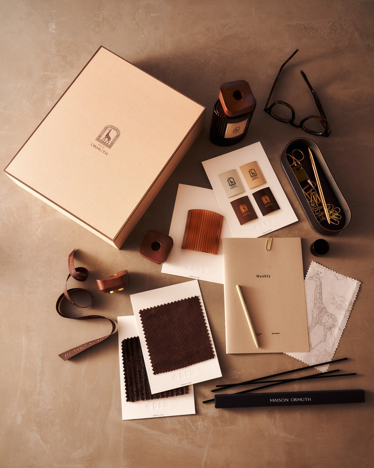 The Maison Ormuth gift box open, its contents laid out: vessel, cards, ribbon, fabric swatches and reeds