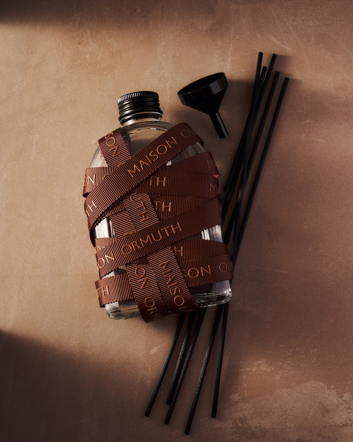 Refill bottle wrapped in Maison Ormuth ribbon, with a metal funnel and black reeds