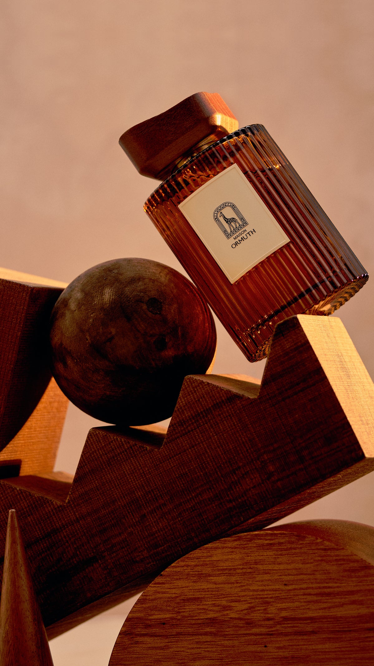 Maison Ormuth reed diffuser vessel resting on a stack of carved walnut blocks against a plaster wall