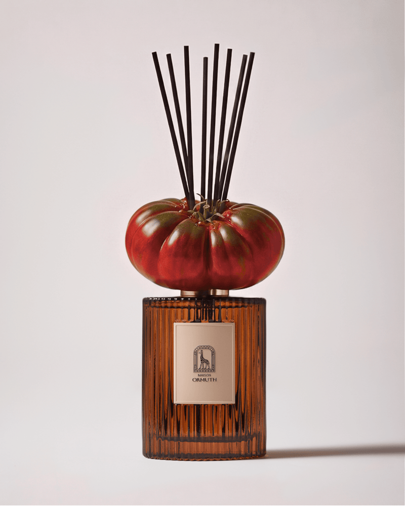 Imperial Tomato reed diffuser by Maison Ormuth: ribbed amber glass vessel with black reeds and a ripe tomato resting on the cap